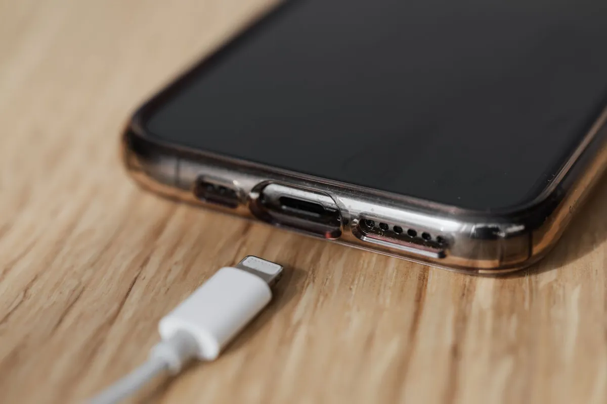 Móvil con funda transparente sobre una mesa de madera cálida con un cable USB blanco conectado al puerto de carga